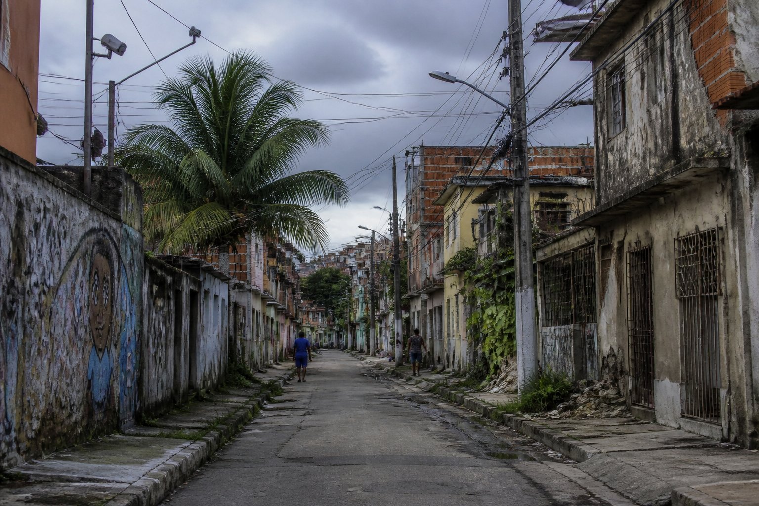 Vista de um bairro urbano em Cabo Frio com ruas estreitas, prédios desgastados e poucas pessoas caminhando com cautela.