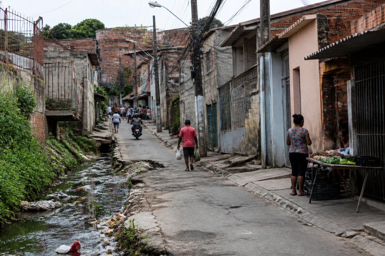 Área urbana de bairro com infraestrutura precária, ruas estreitas, prédios antigos e lixo espalhado.