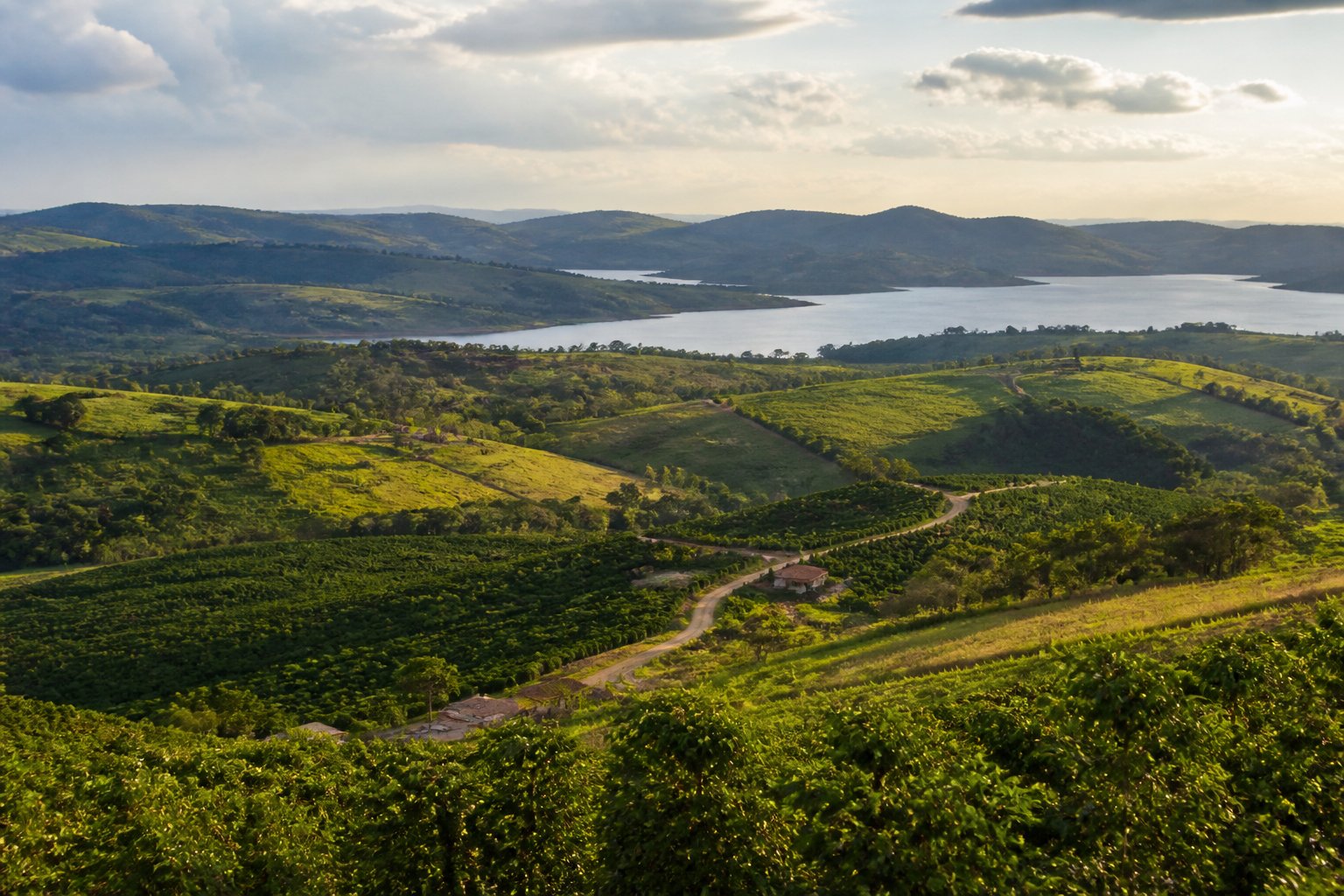 Paisagem de Caconde com colinas verdes, áreas rurais, uma estrada sinuosa e a represa ao fundo.